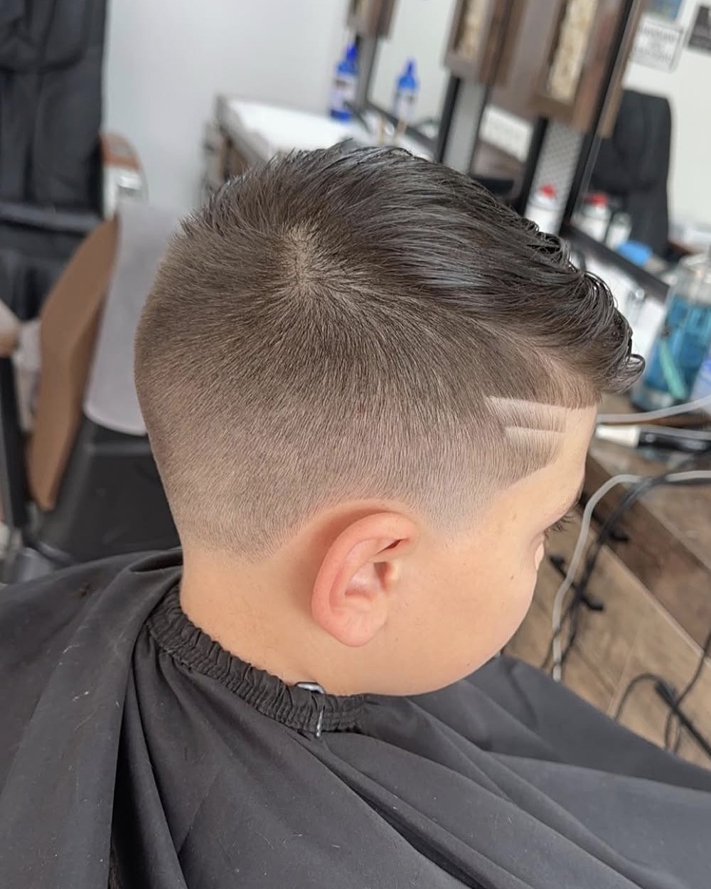 Een jongen met een korte fade en een lijn erin geschoren, van achteren gezien in de stoel